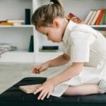 Dziewczynka w białej sukience układa drewniane klocki na dywanie