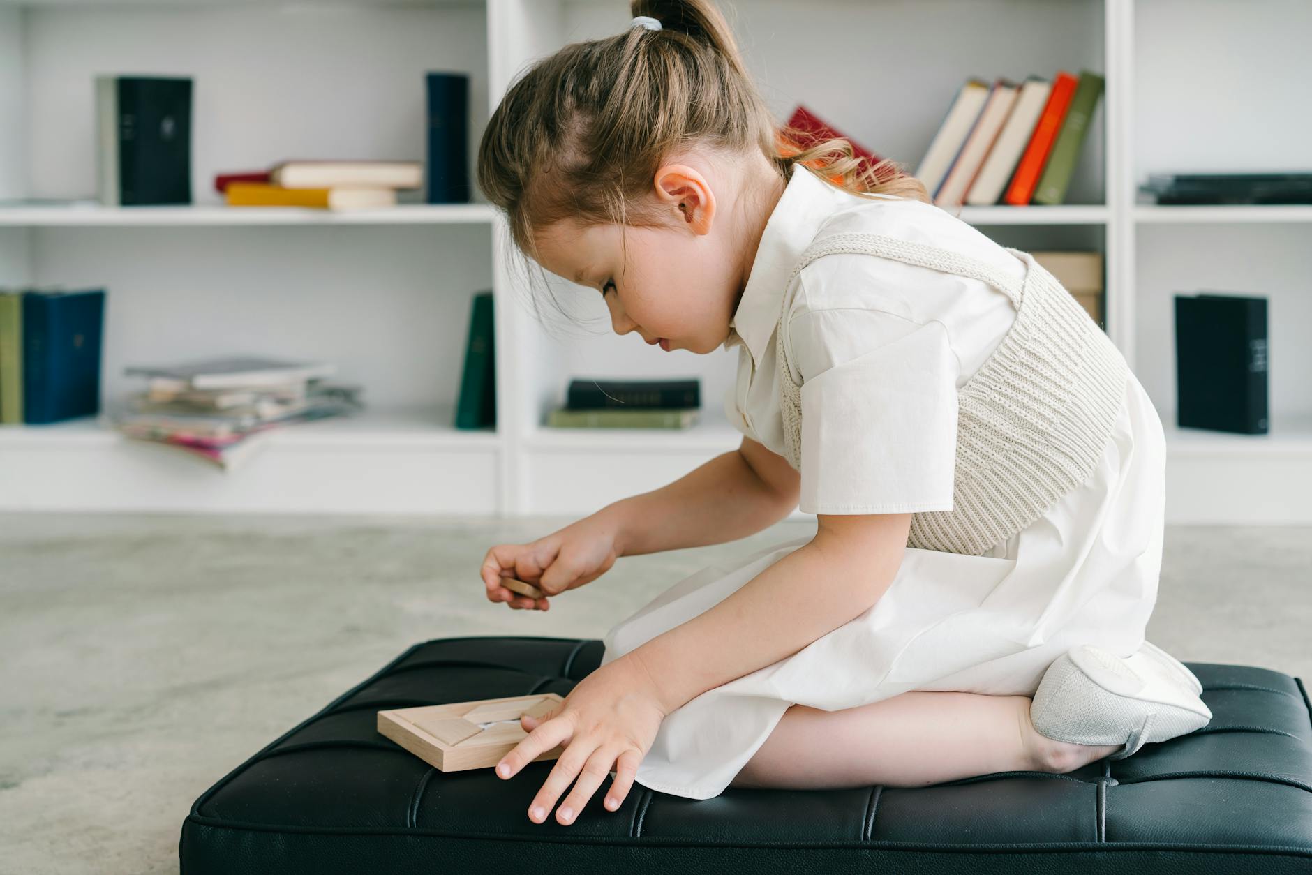 Dziewczynka w białej sukience układa drewniane klocki na dywanie