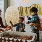 Mama bawi się z dwójką dzieci pacynkami w kąciku zabaw na dywanie