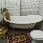 Wanna z nóżkami i wzorzysty dywanik w jasnej łazience z płytkami