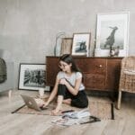 Kobieta boso czyta na laptopie, siedząc na dywanie w eko salonie
