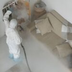 Osoba w kombinezonie ochronnym dezynfekuje wnętrze mieszkania